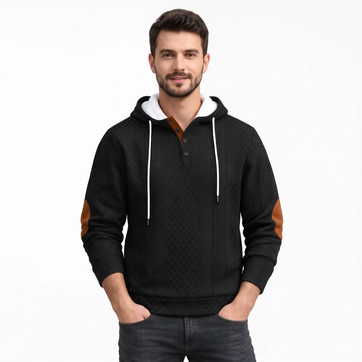 Man in black textured diamond-pattern hoodie with white drawstrings, button placket and brown elbow patches, hands in 41