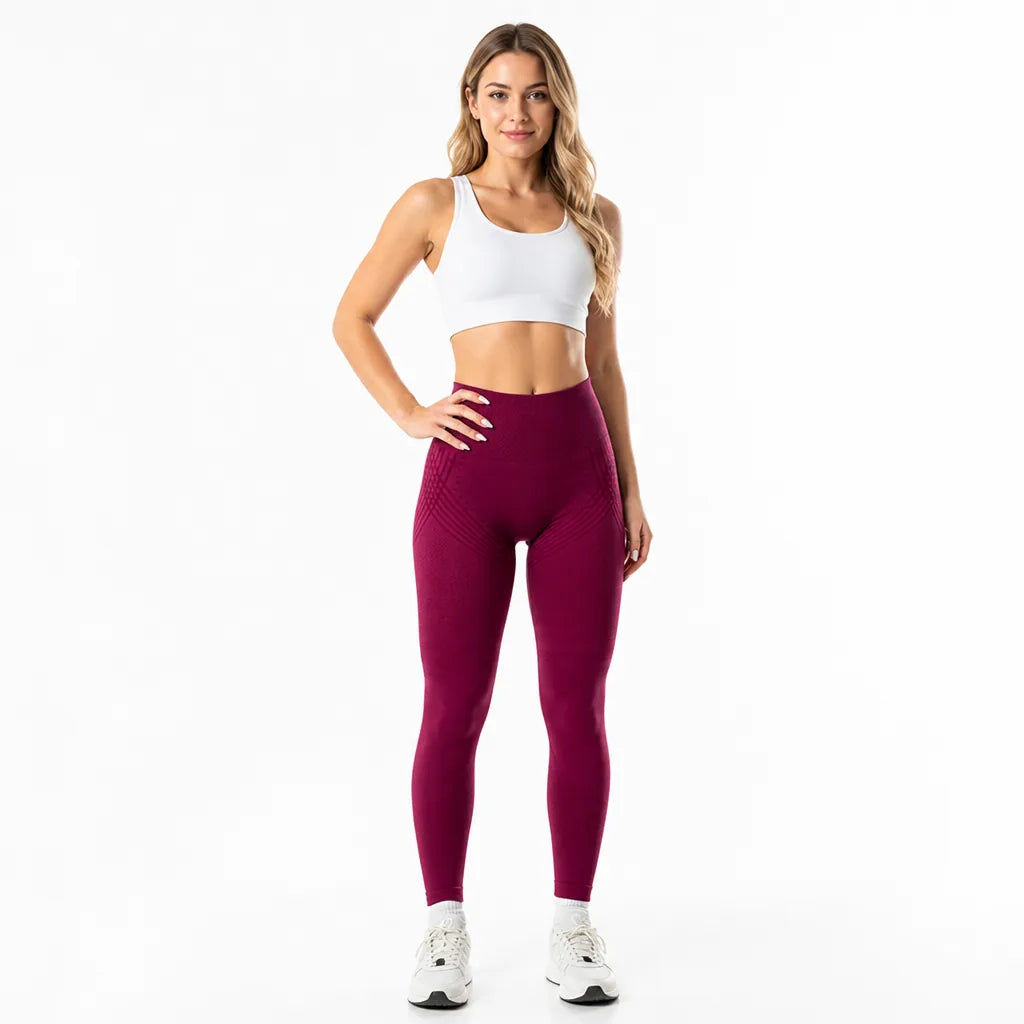 Front view of a model in deep burgundy high-waisted leggings with subtle diagonal lines at the hips, a white sports bra, and sneakers. 15