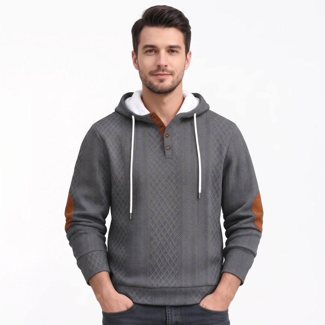 Man in gray diamond-textured hooded sweatshirt with white drawstrings, brown-trimmed buttons and brown elbow patches, hands 43