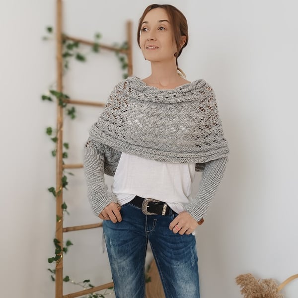 Woman wears the light gray wrap with sleeves, standing with hands in her jeans pockets beside a leafy ladder. 8