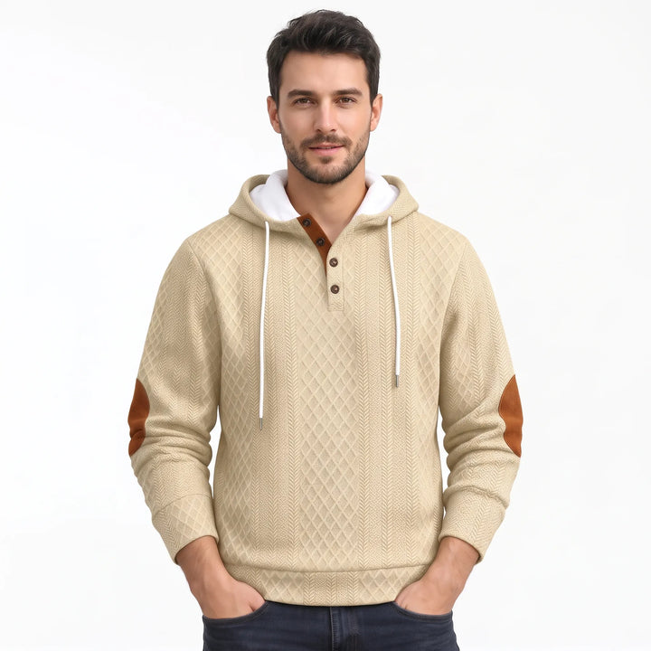 Man wearing beige diamond-textured hoodie with white drawstrings, brown button placket and brown elbow patches, standing with 44