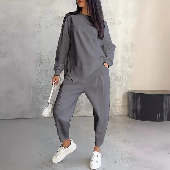 Woman wearing the gray version of the matching sweatshirt and joggers, hand in pocket, styled with white sneakers.