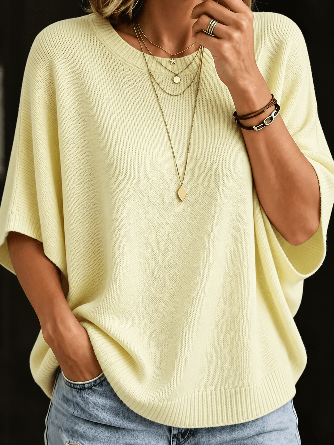 Pale yellow knit batwing top, close-up front view with ribbed round neck and layered necklaces.