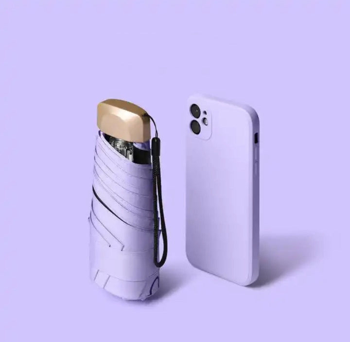 Folded lavender umbrella with a gold cap and wrist strap beside a lavender smartphone on a purple background.