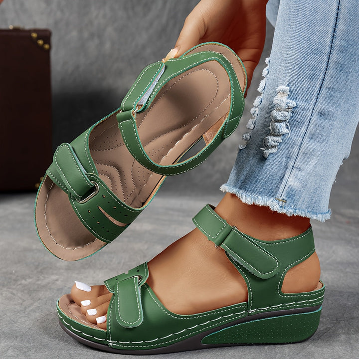 Green wedge sandal with white stitching and hook-and-loop straps, with the insole visible. 3