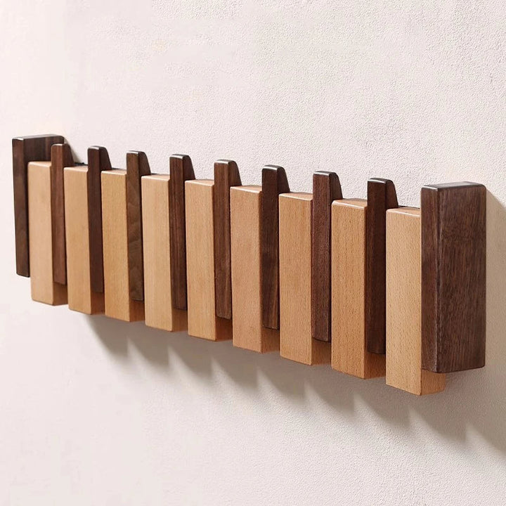 Angled view of the empty rack in alternating dark and light wood slats, hooks folded flat, mounted on a beige wall.