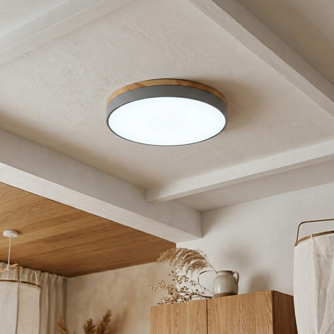 Gray disc ceiling light with wood-grain trim shining bright cool white on a beamed plaster ceiling. 16