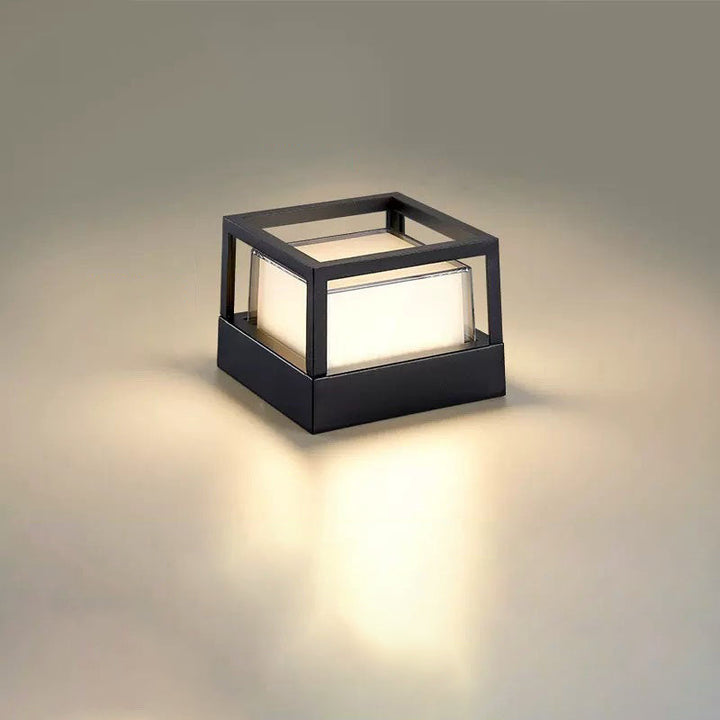 Square black lamp with an open cage top frame and glowing frosted block diffuser, casting warm light on a neutral surface. 11