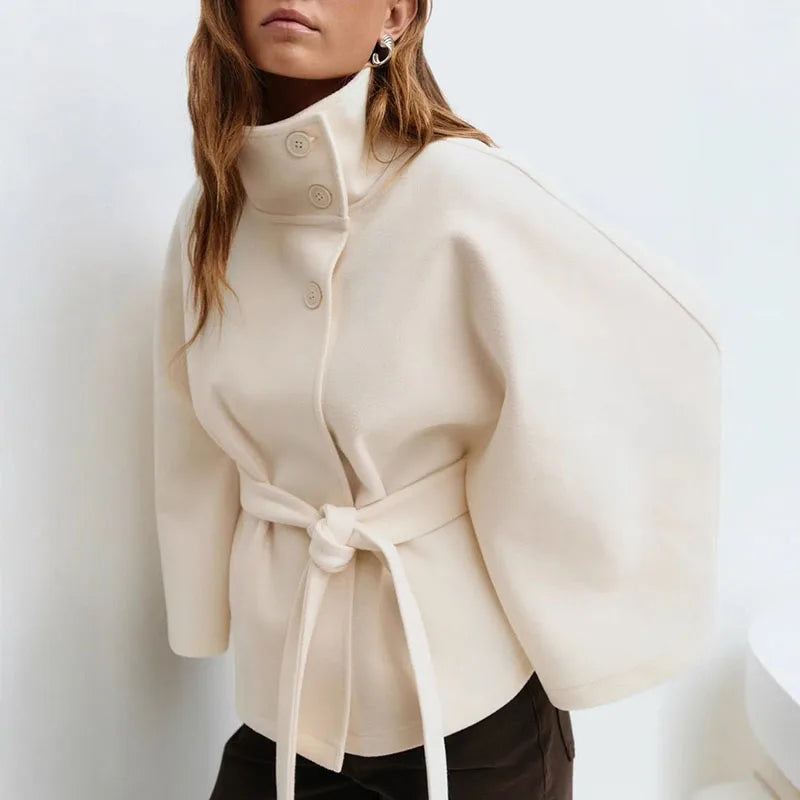 Cream cape jacket worn by a model in three-quarter view, belt knotted at the waist 4