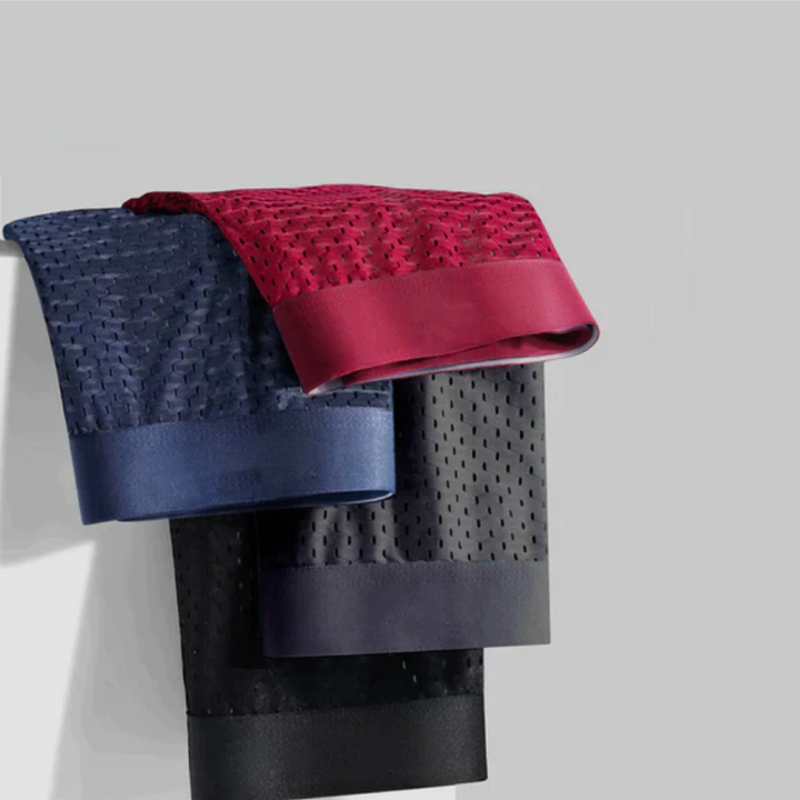 Navy, red, gray and black perforated mesh boxers folded and draped over a ledge against a light gray wall 3