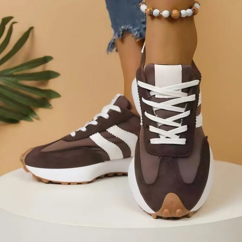 Front view of brown platform trainers with white stripes and crisscross laces, worn on a white pedestal 4