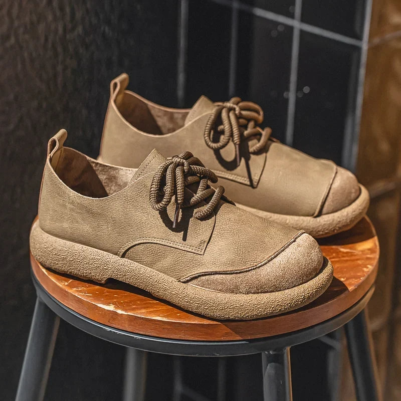 Khaki lace-up shoes with suede toe caps and crepe-style soles, displayed on a wooden stool 4