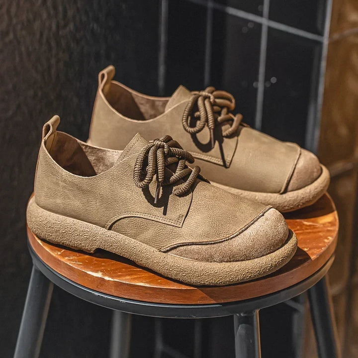 Khaki lace-up shoes with suede toe caps and crepe-style soles, displayed on a wooden stool 4