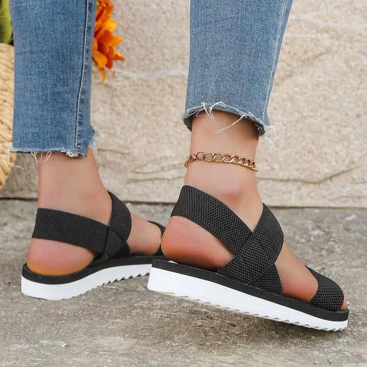 Rear view of black sandals showing the crossed elastic heel straps and white ridged platform sole 4