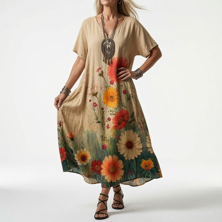 Woman wearing a beige V-neck dress with large orange, red and yellow daisies that fade into green toward the hem.