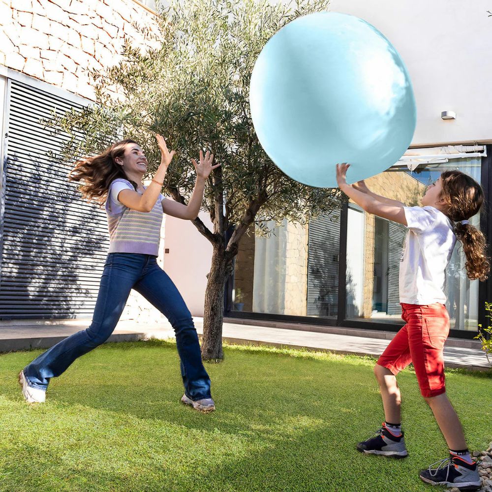 A woman and a girl toss a large light blue balloon ball back and forth on a sunny backyard lawn. 2