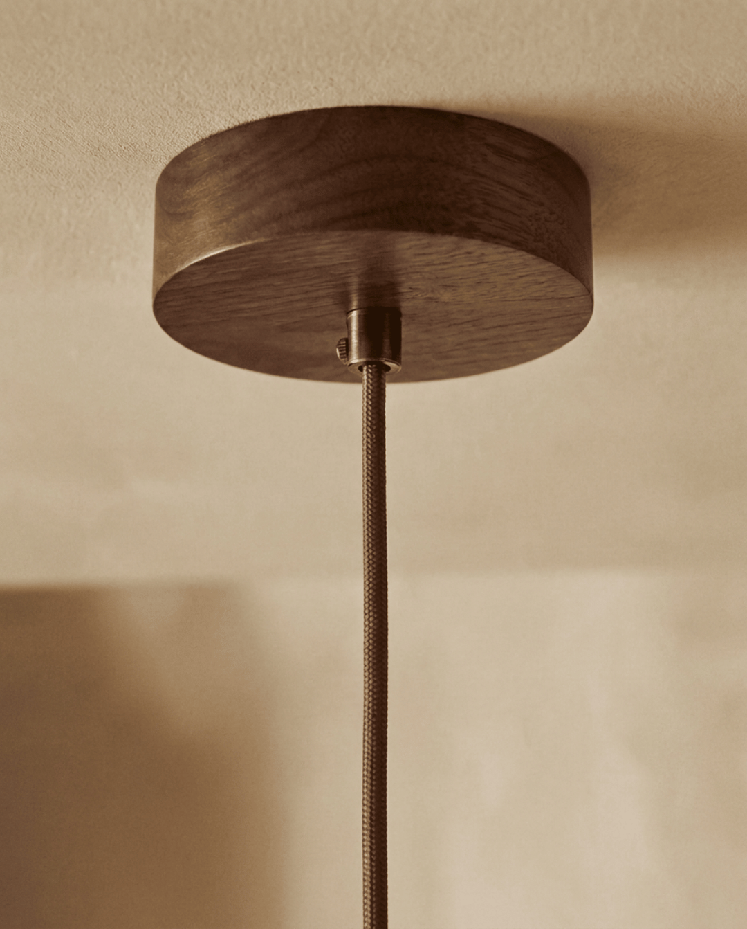 Travertine pendant light detail of the round dark wood ceiling canopy and braided brown cord.