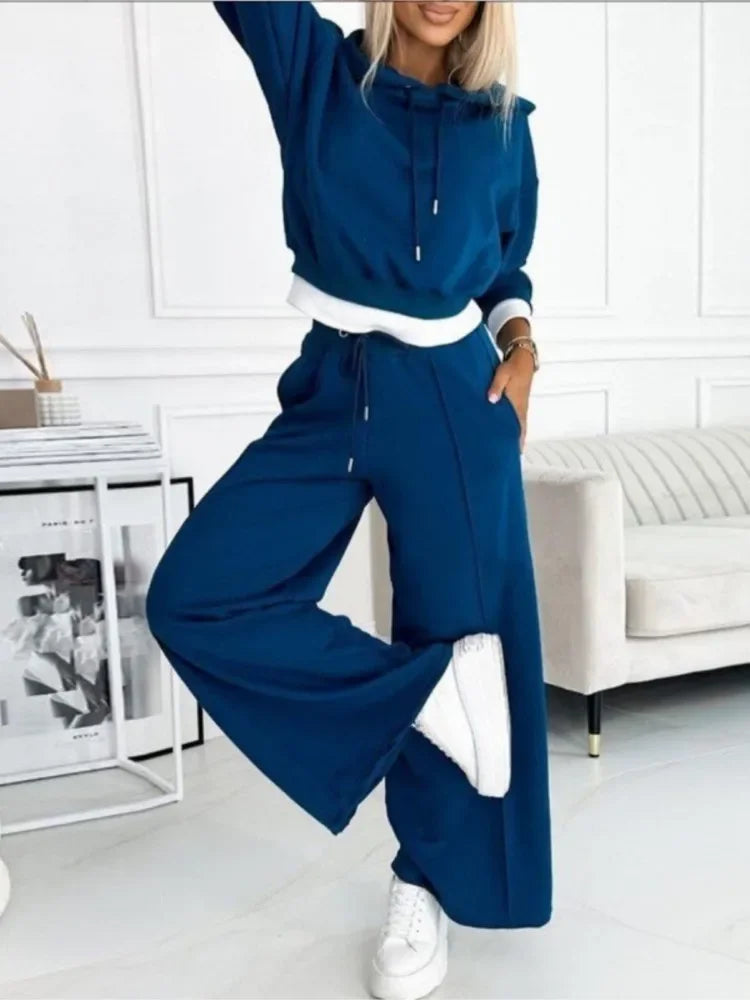 Model in a deep blue hoodie and pants with white trim, one leg raised, hand in pocket 4