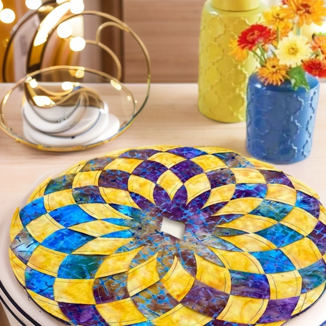 Close view of a yellow, blue and purple spiral-patterned placemat beside blue and yellow vases of flowers.