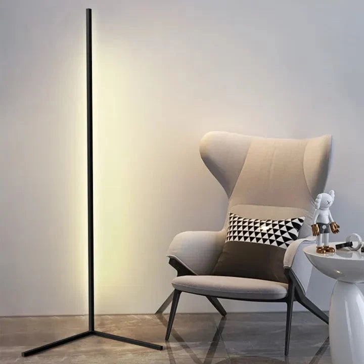 Black corner floor lamp with a warm glow standing next to a cream wingback armchair with a patterned cushion and a white side table. 6