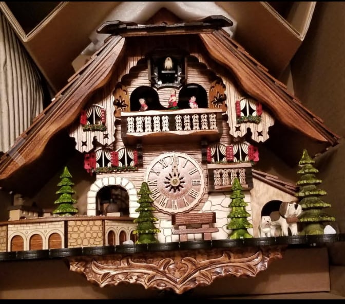 Chalet clock partly unpacked in its shipping box, showing carved base, balcony figures, trees and dogs 14
