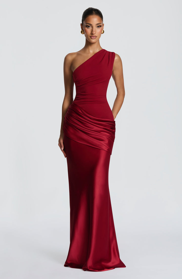 Deep red one-shoulder gown shown straight on with hands at the hips, emphasizing the draped satin wrap. 17