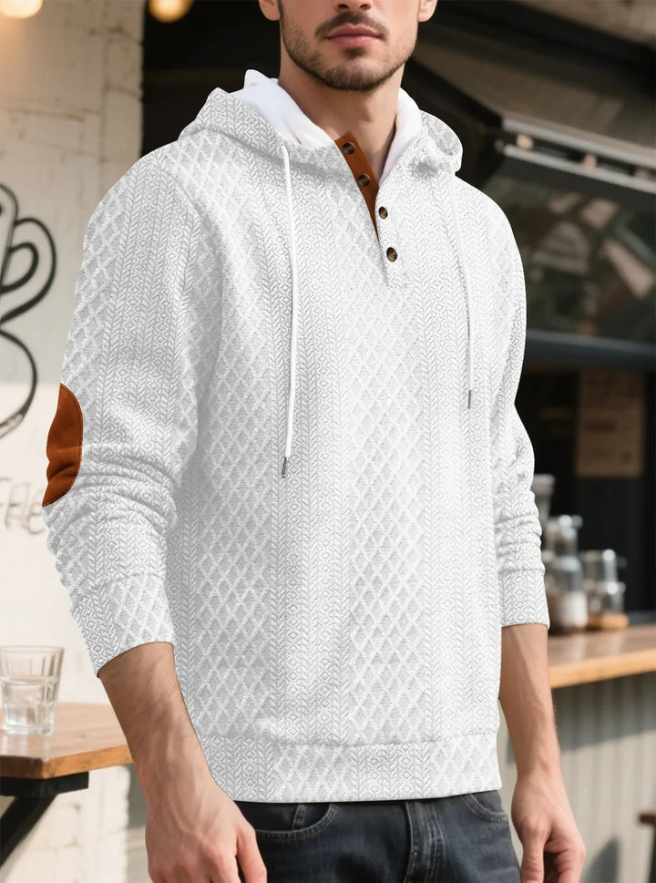Man wearing a white diamond-textured hoodie with brown elbow patch and buttons, standing near a cafe counter 5