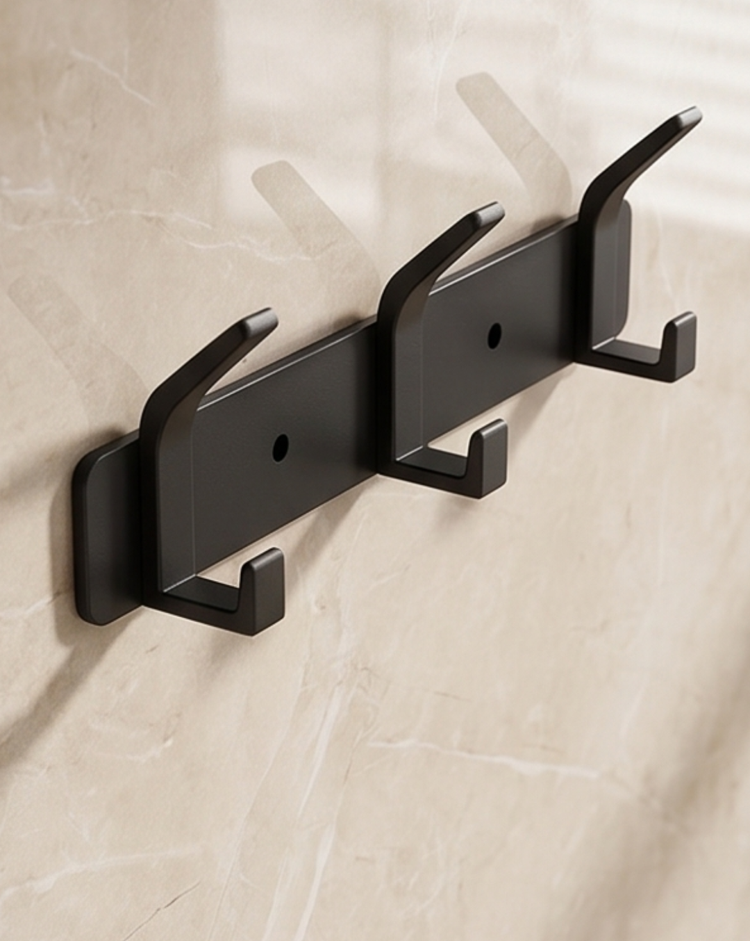 Black three-hook rack, another view, mounted on a marble-look wall with screw holes visible.