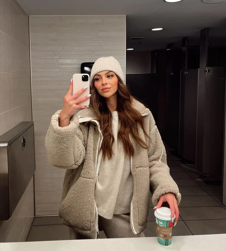 Woman taking a mirror selfie in a taupe fleece coat, cream beanie and cozy knit loungewear 5
