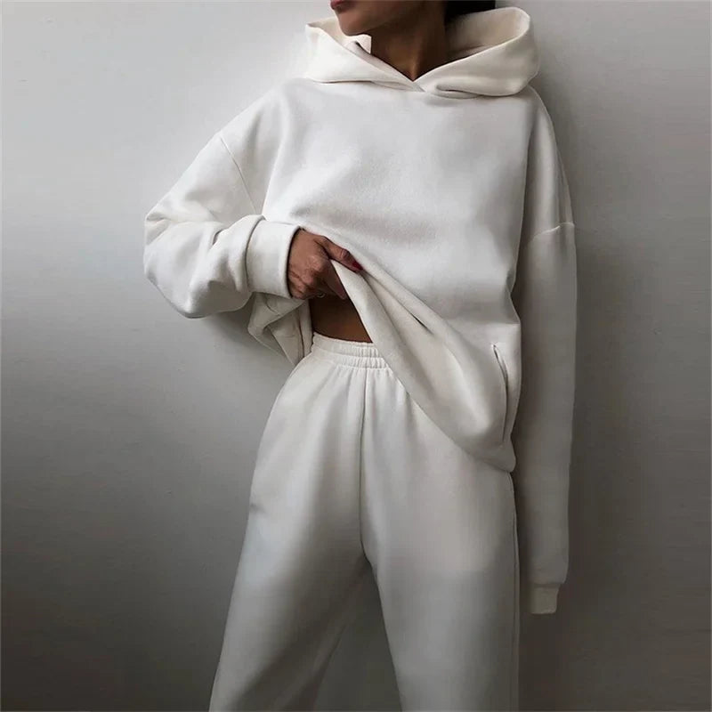 Model in the white oversized hoodie and matching pants, tugging the hem, with a side pocket visible 5