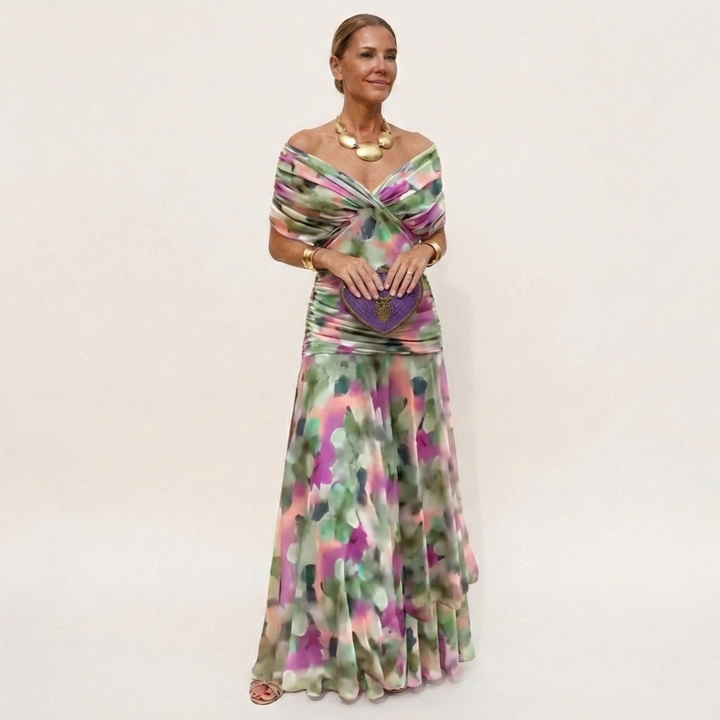 Model in a long off-the-shoulder dress with a blurred green, pink and purple watercolor print, holding a purple heart clutch. 6