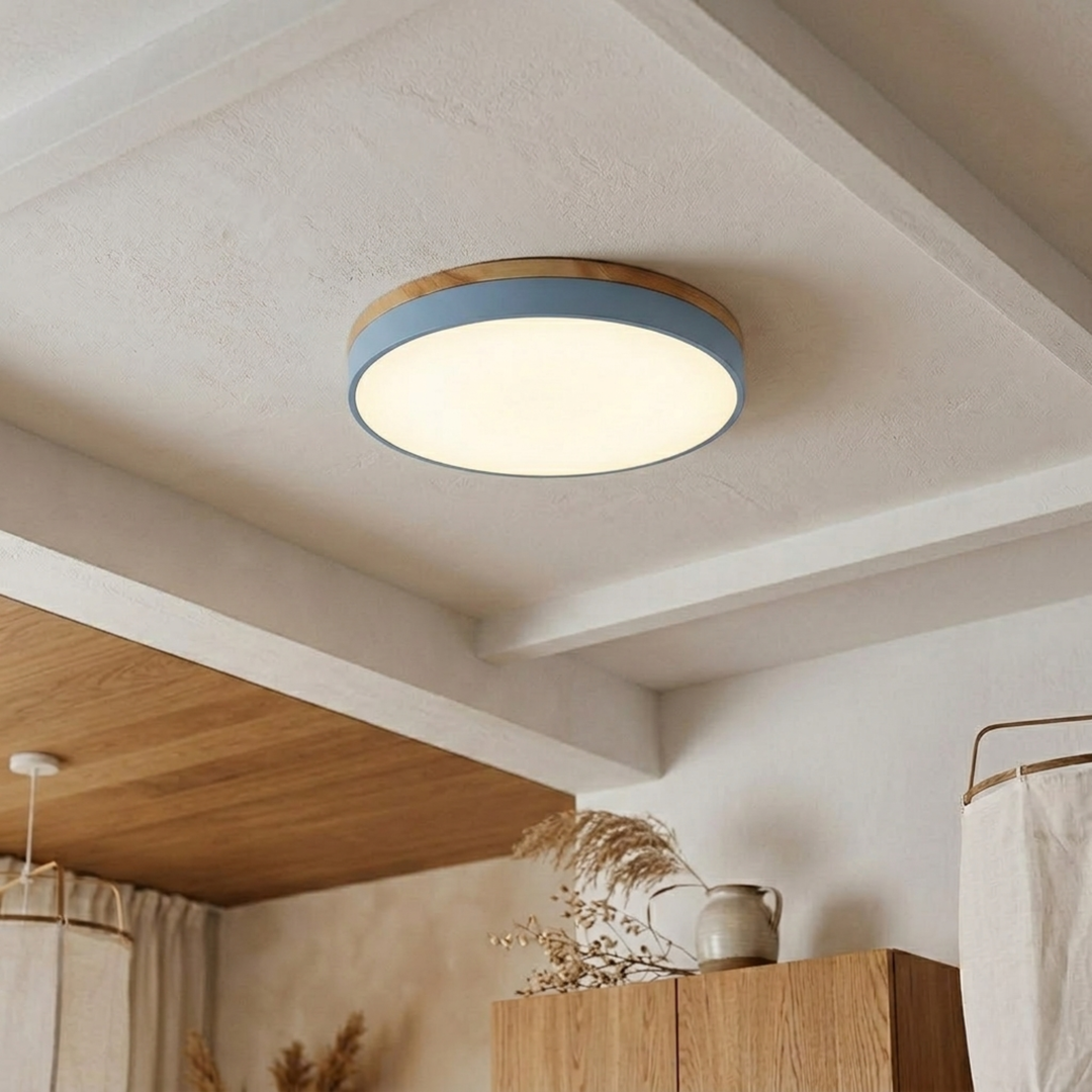 Light blue disc ceiling light with wood-grain trim glowing warm white on a beamed plaster ceiling. 13