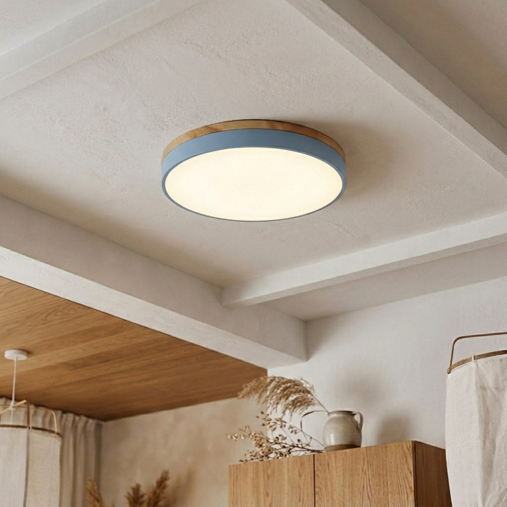 Light blue disc ceiling light with wood-grain trim glowing warm white on a beamed plaster ceiling. 13