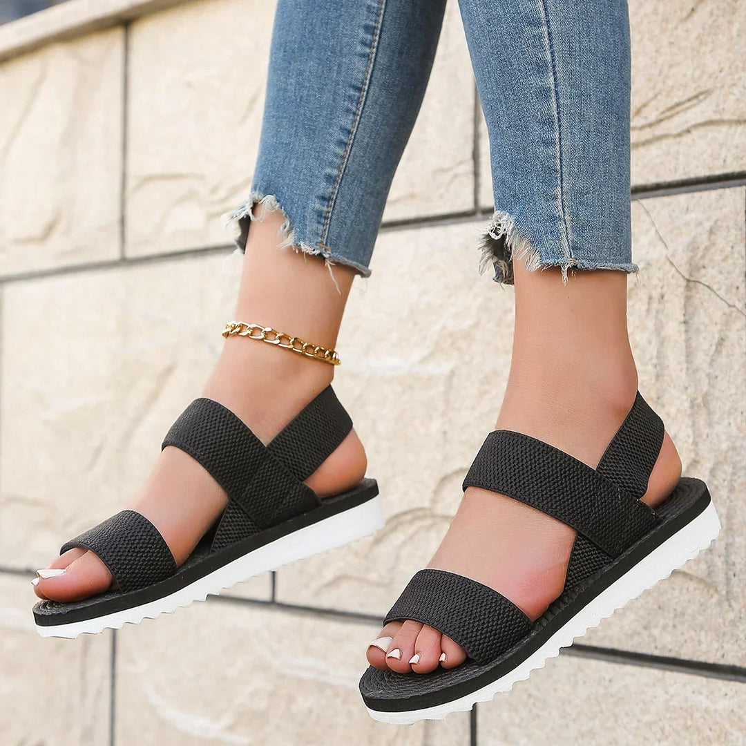 Black elastic sandals worn with cropped jeans, feet dangling in front of a pale brick wall 5