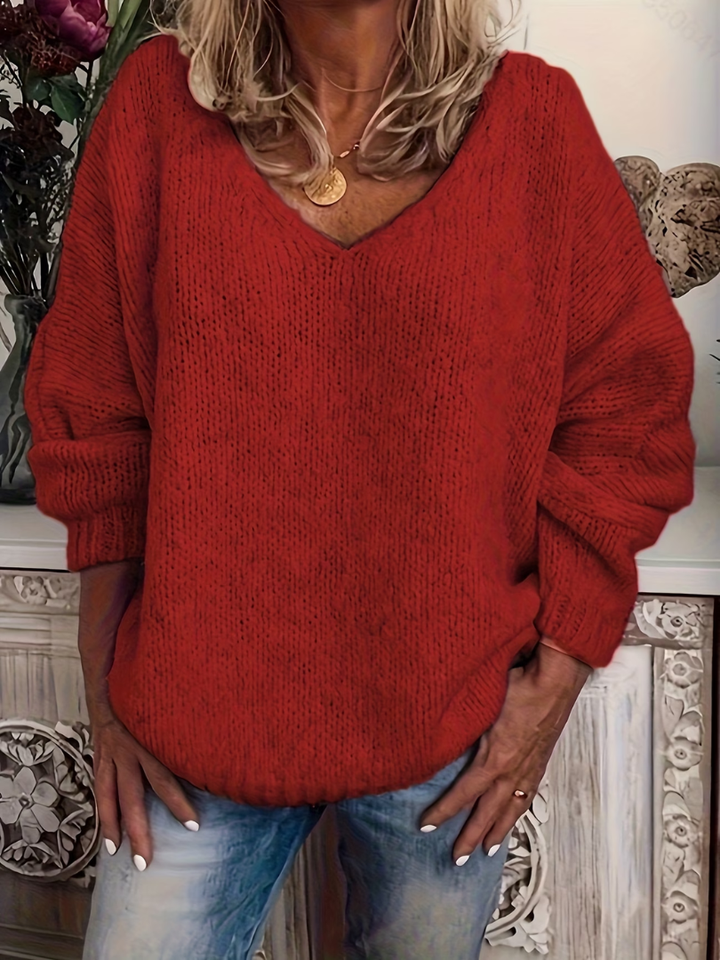 Relaxed-fit V-neck knit sweater in red worn by a model, showing the chunky stitch and ribbed cuffs.