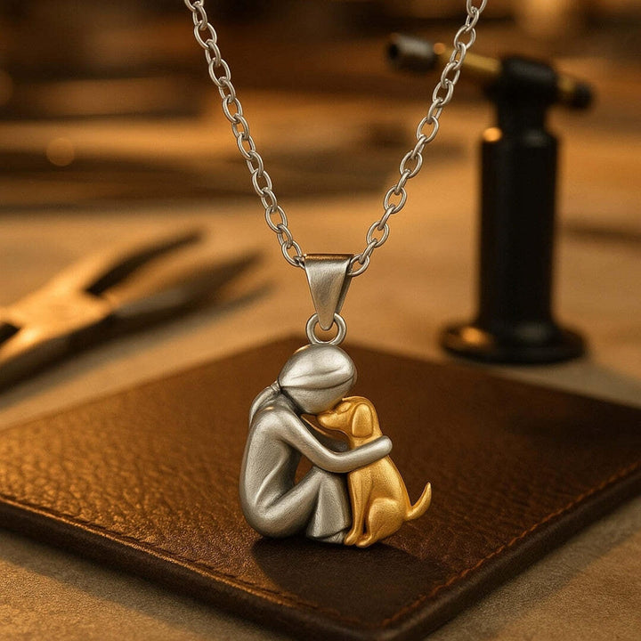 Silver-tone pendant of a seated figure hugging a golden dog on a brown leather surface.