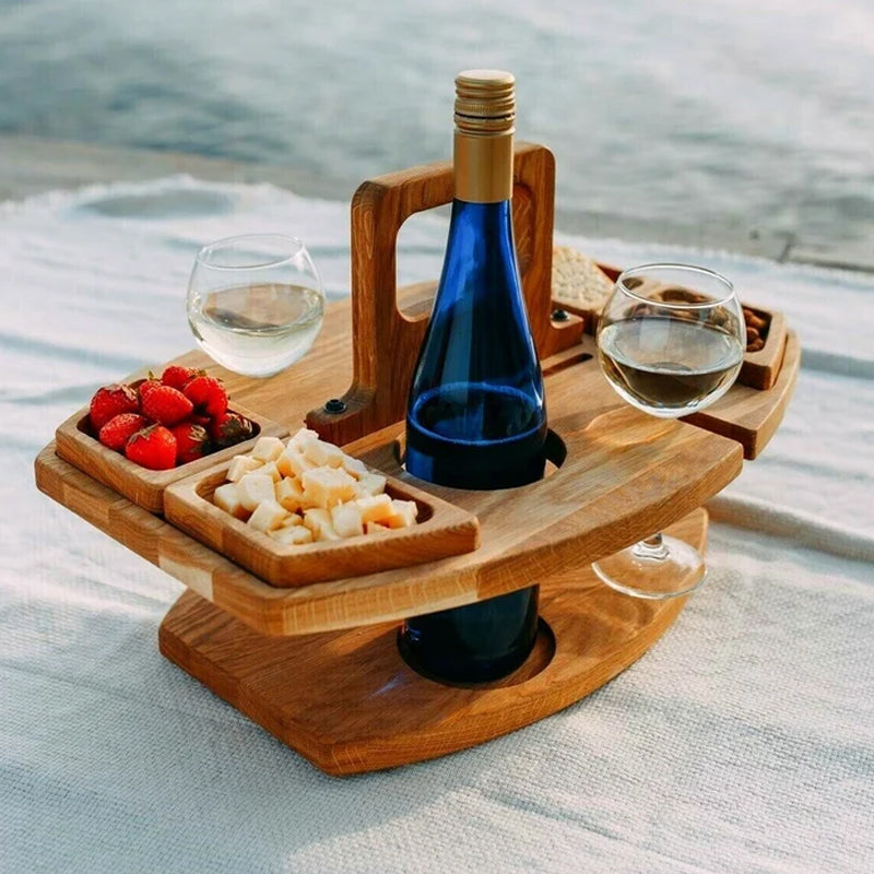 Wooden picnic table on a blanket holding a blue wine bottle, two glasses, strawberries, cheese and nuts 1