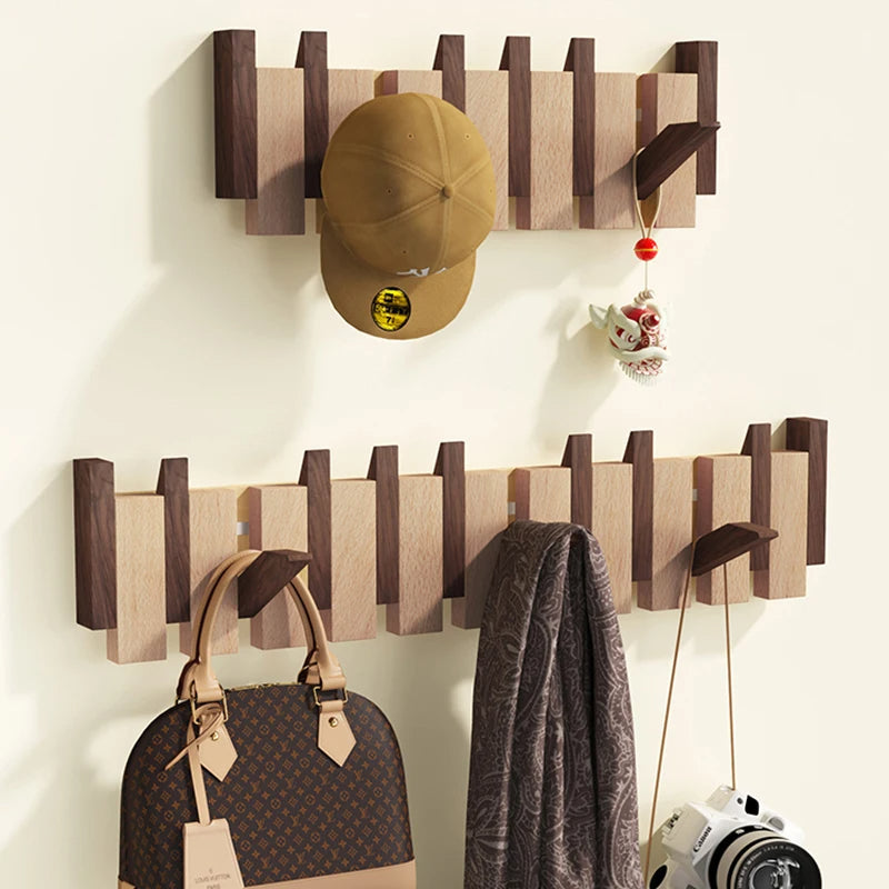 Two-tone wood racks on a cream wall holding a cap, a handbag, a patterned scarf and a camera.