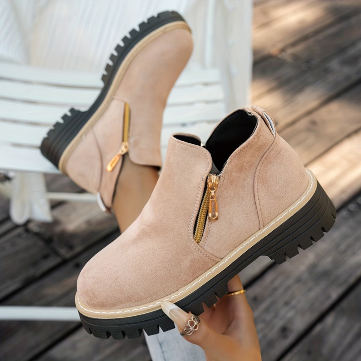 Light blush beige suede-look ankle boots with gold side zippers and chunky black lug soles.