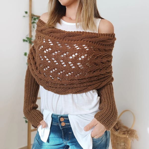 Front view of the brown wrap worn off the shoulders, showing the zigzag lace pattern and ribbed sleeves with hands in jeans pockets. 18