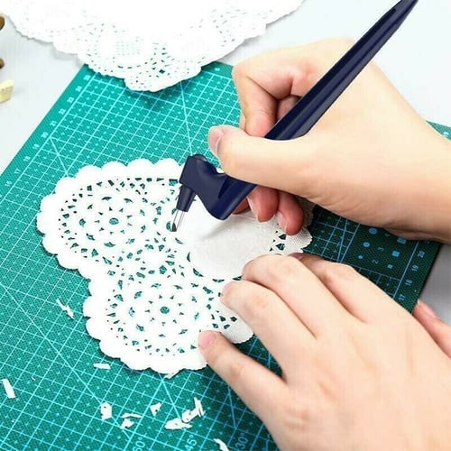 Two hands cutting a white heart-shaped lace paper doily on a green mat with the navy knife, paper scraps around. 4