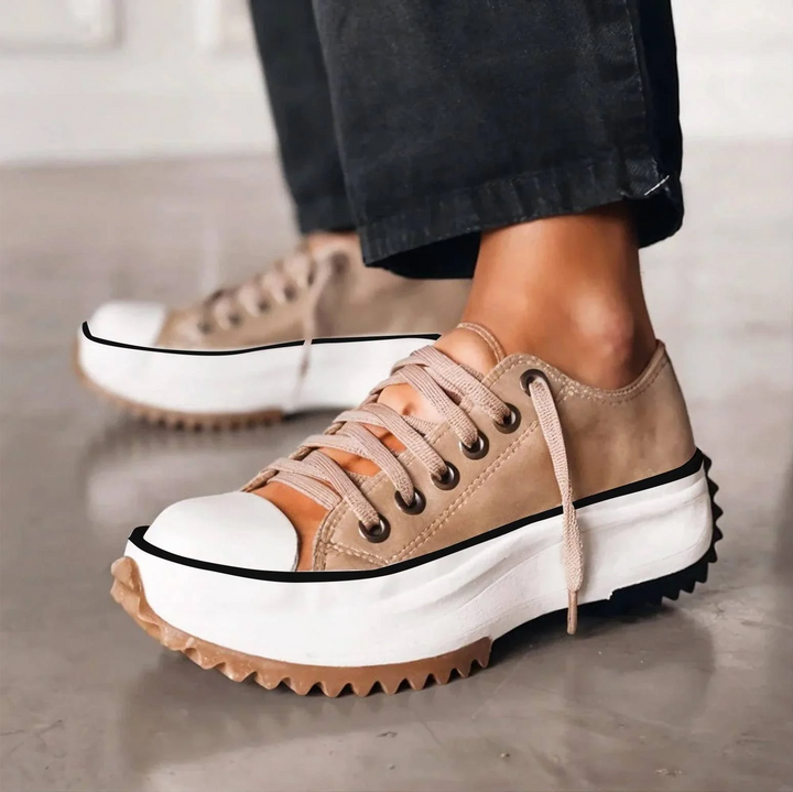 Side view of tan lace-up platform sneakers with a white chunky sole and serrated gum edge, worn with black pants. 1