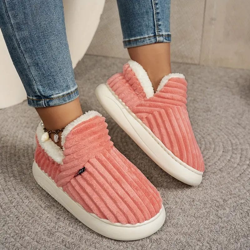 Angled view of coral pink ribbed slippers worn with rolled jeans on a gray rug, showing the thick white sole.