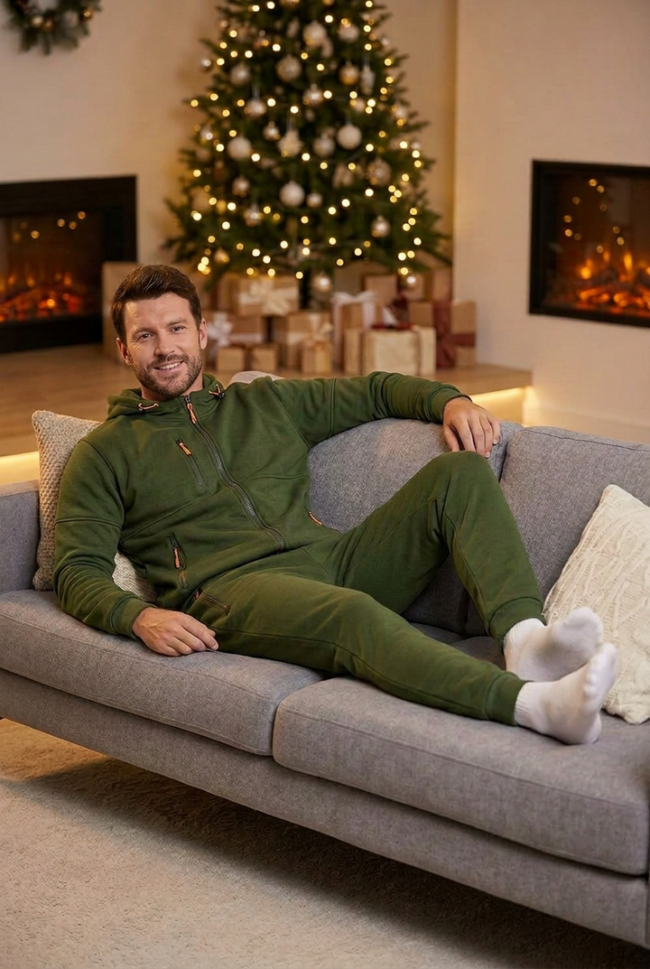 Smiling man in an olive green hooded zip set relaxes on a gray sofa by a Christmas tree 1