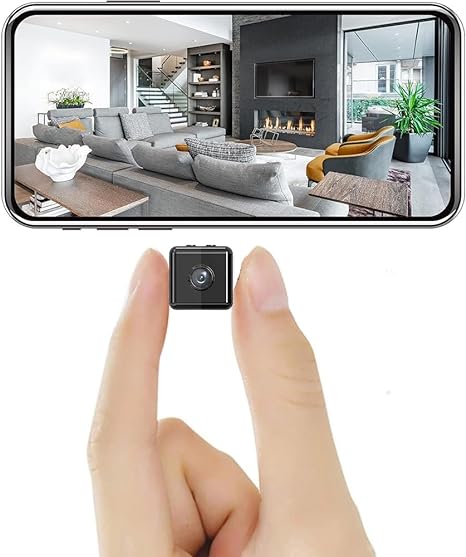 Tiny black cube camera held between two fingertips to show its size, with a phone above displaying a living room view. 1