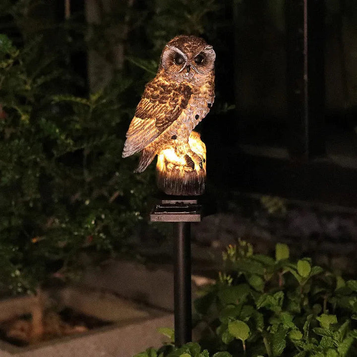 Brown owl light lit at night on a stake, surrounded by dark garden foliage 4