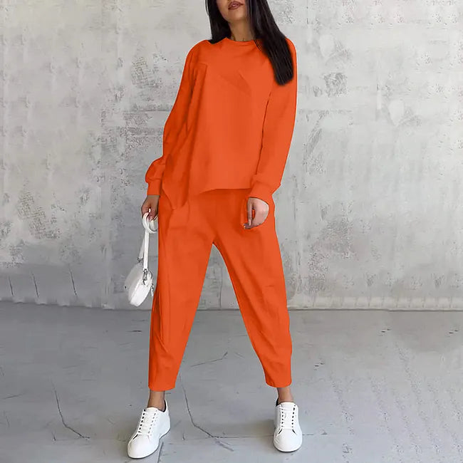 Woman wearing the bright orange sweatshirt and jogger pants with white sneakers, holding a small white bag.