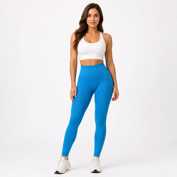 Full-length front view of a model in bright blue high-waisted leggings with a white sports bra and white sneakers. 12