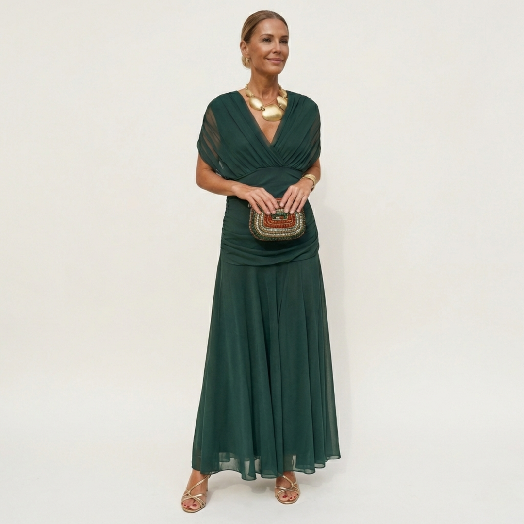Model in a dark green chiffon maxi dress with a gathered V-neck bodice, holding a beaded clutch and wearing gold jewelry. 1