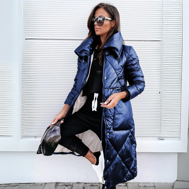 Long quilted puffer coat in glossy navy blue with a high collar, worn open over black.